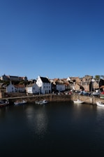 Crail harbour white and brown concrete buildings beside body of water under blue sky during daytime