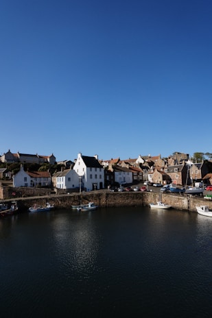 Crail harbour white and brown concrete buildings beside body of water under blue sky during daytime