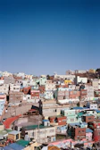 A lively street scene in a Rio favela with colorful houses stacked on a hillside under a bright sky.