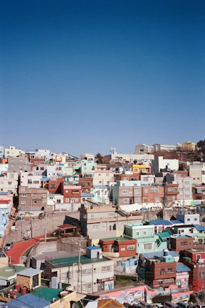 A lively street scene in a Rio favela with colorful houses stacked on a hillside under a bright sky.