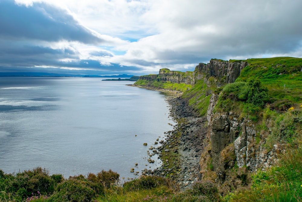 green and brown cliff beside body of water under white clouds and blue sky during daytime