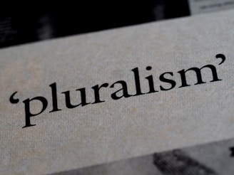 The word 'pluralism' is printed in bold black text on a textured, light-colored background. The texture of the paper and the sharpness of the text are in focus.
