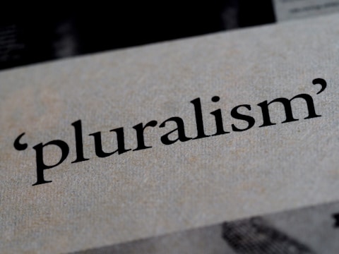 The word 'pluralism' is printed in bold black text on a textured, light-colored background. The texture of the paper and the sharpness of the text are in focus.