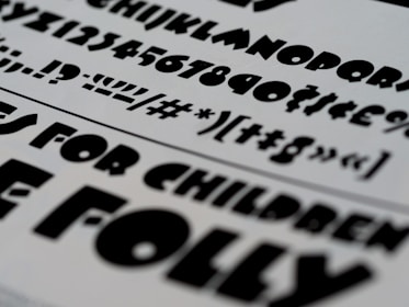 A selection of bold, black typography on a white paper background, featuring a variety of fonts and characters. These include uppercase and lowercase letters, numbers, and symbols.