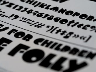 A selection of bold, black typography on a white paper background, featuring a variety of fonts and characters. These include uppercase and lowercase letters, numbers, and symbols.