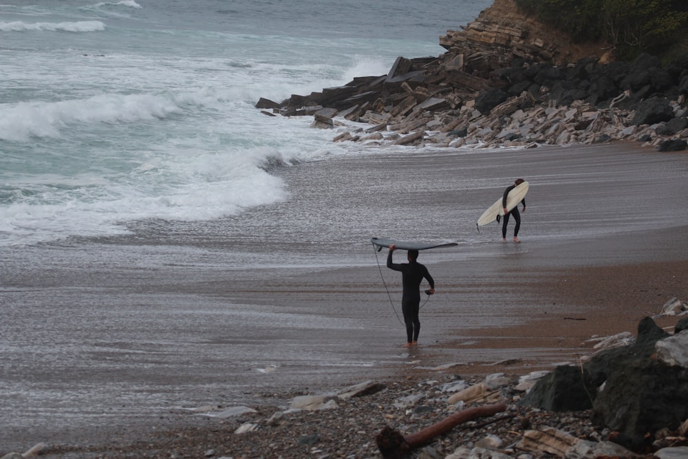 2 person holding surfboard walking on seashore during daytime