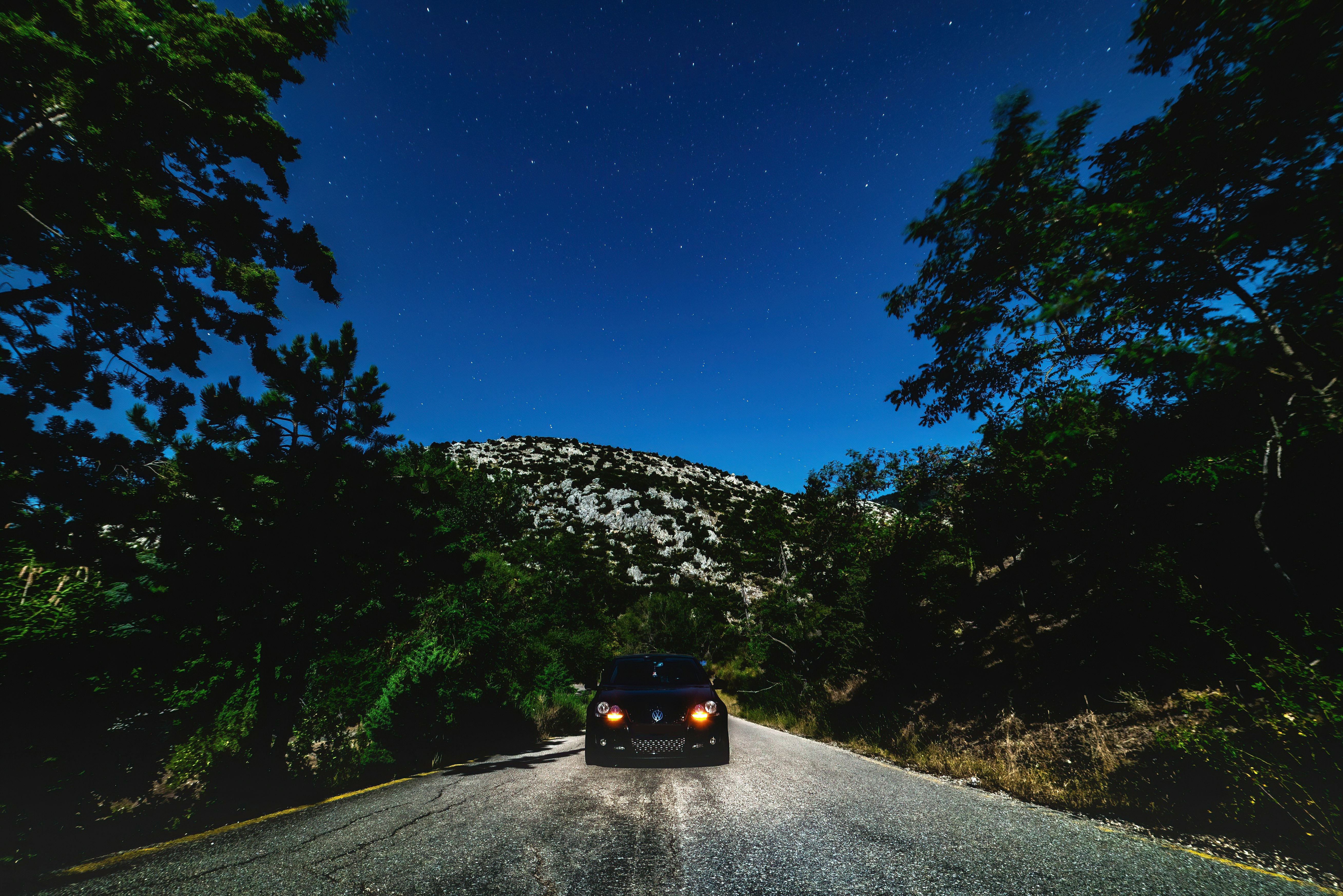 black car on road between trees during daytime