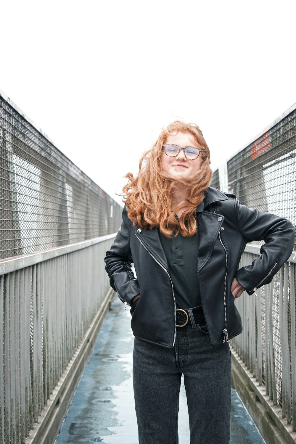 woman in black leather jacket standing on bridge during daytime