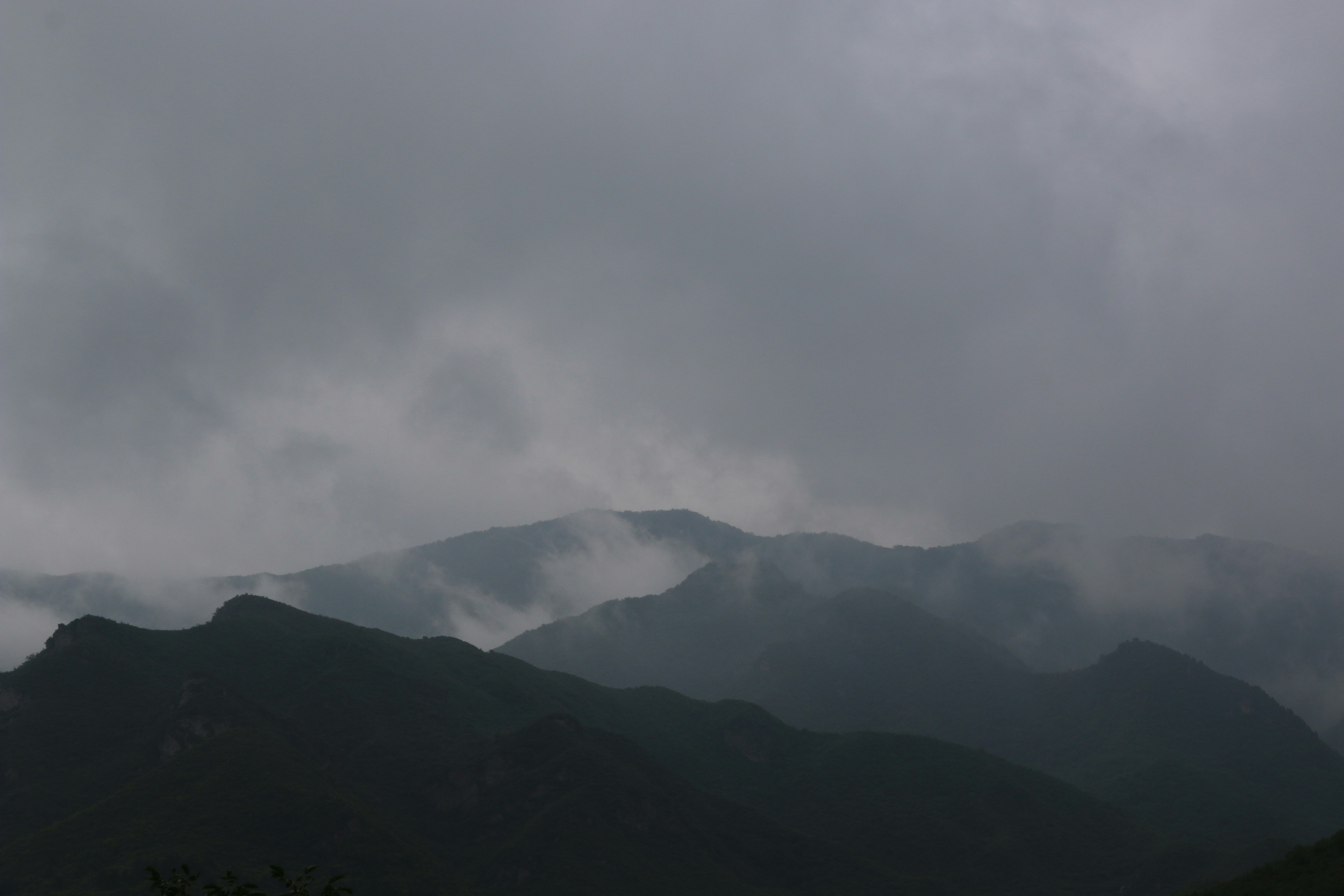 Vast mountainous landscape shrouded in dark mist and storm clouds, deep shadows, dramatic low-key atmospheric lighting