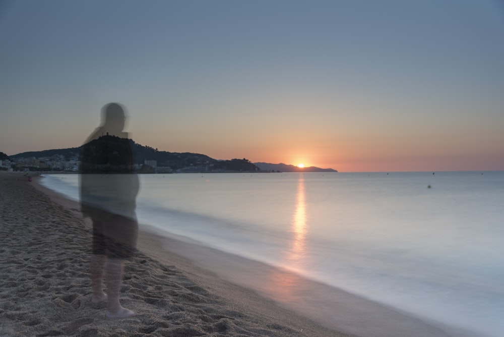 Persona sentada en la orilla de la playa durante la puesta del sol
