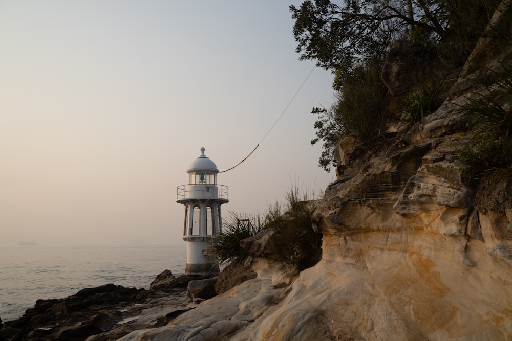 white and black lighthouse on brown rocky mountain near body of water during daytime