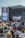 A large outdoor music festival with a crowd seated on the grass, facing a stage with a large screen displaying a musician. The stage is set up with banners that read 'Pori Jazz 2019' and 'International Jazz Festival Every Year in July'. The audience is a mix of standing and seated individuals, many of whom are using picnic chairs. The atmosphere is casual and relaxed.
