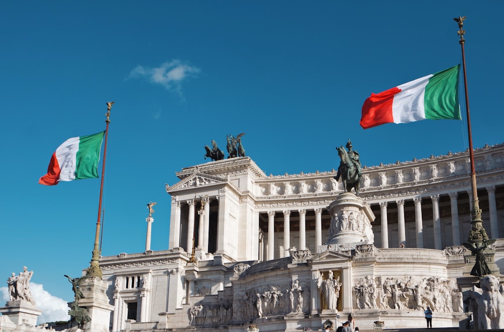 Edificio de hormigón blanco con bandera roja en la parte superior bajo el cielo azul durante el día