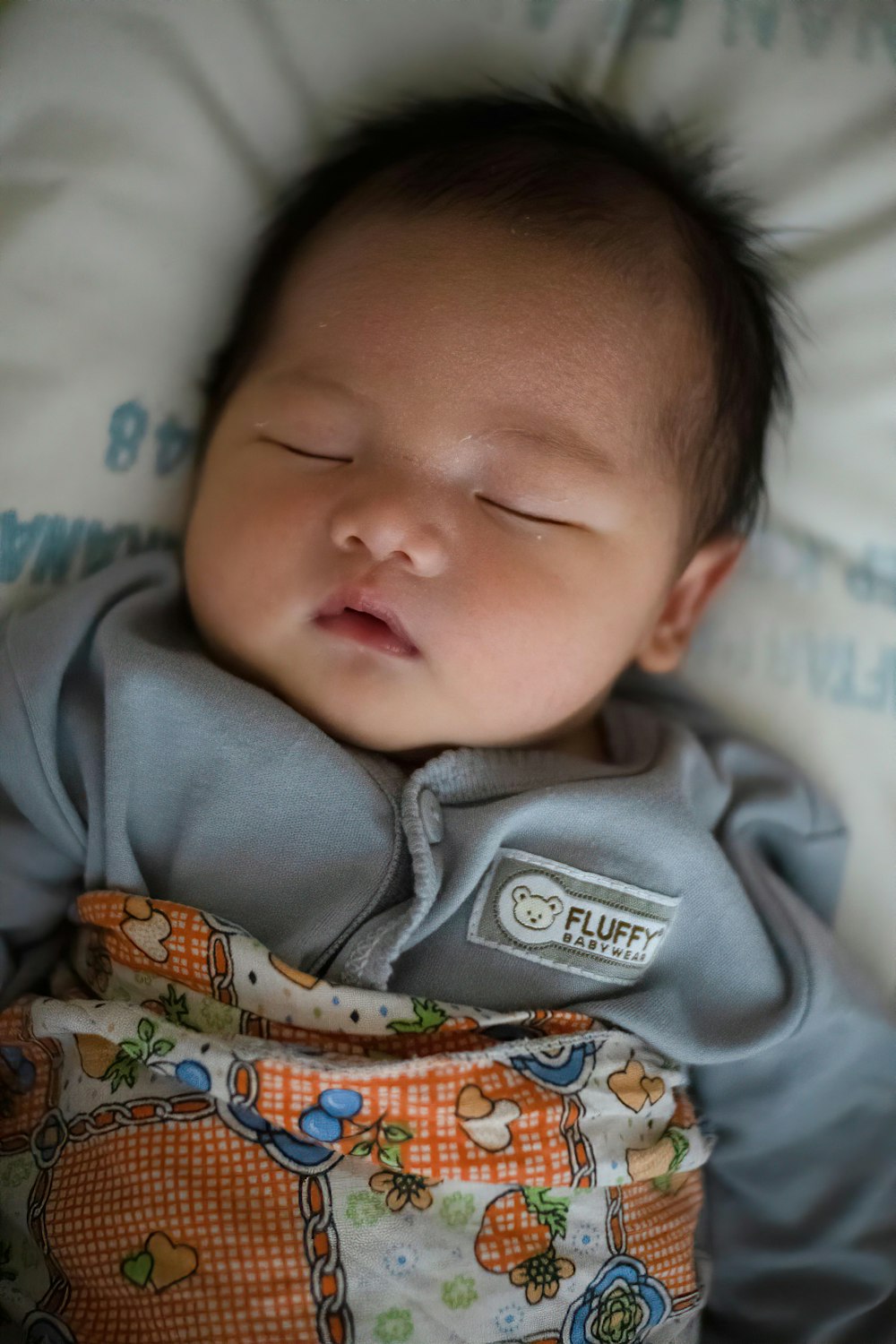 baby in gray onesie lying on bed