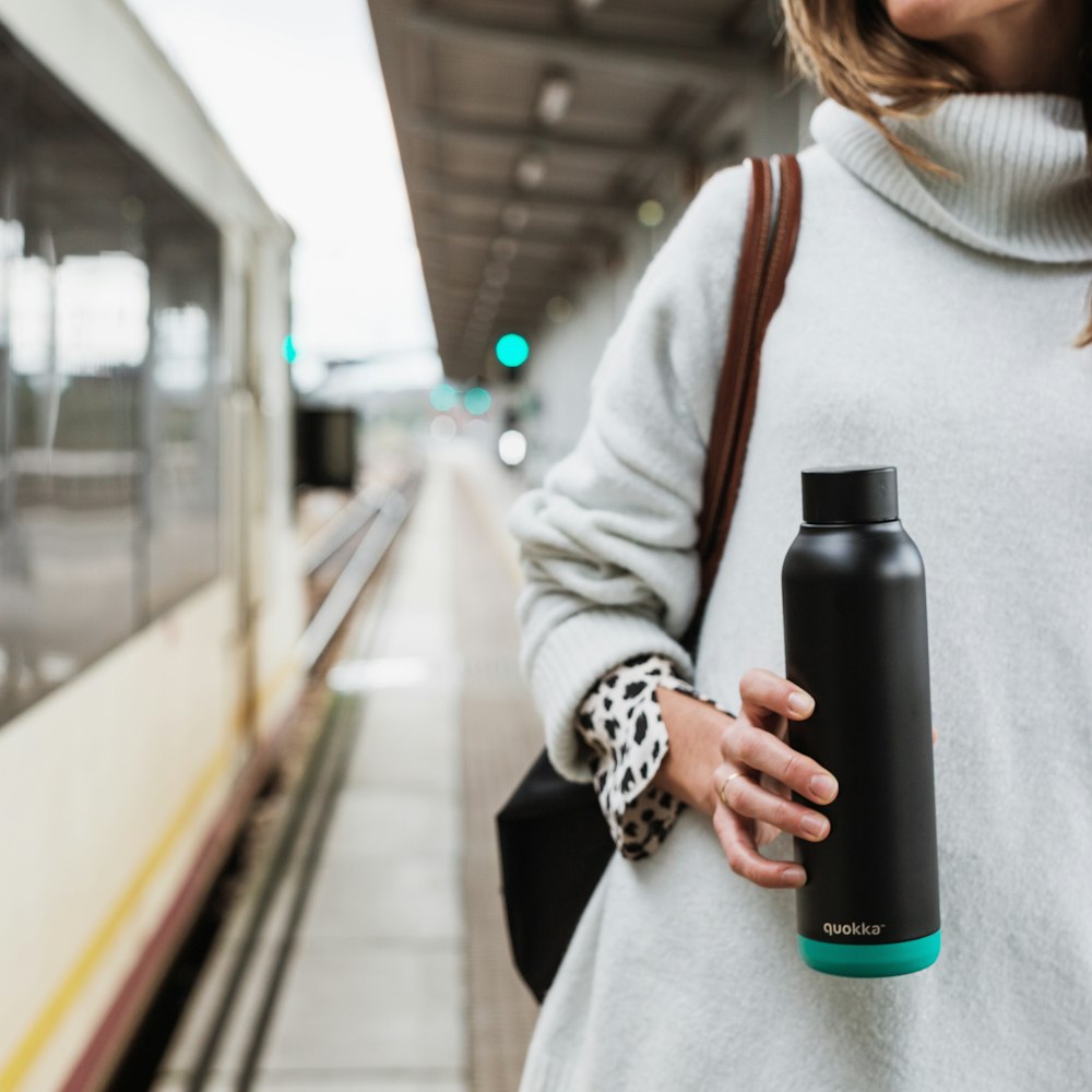 woman in white coat holding black and blue bottle