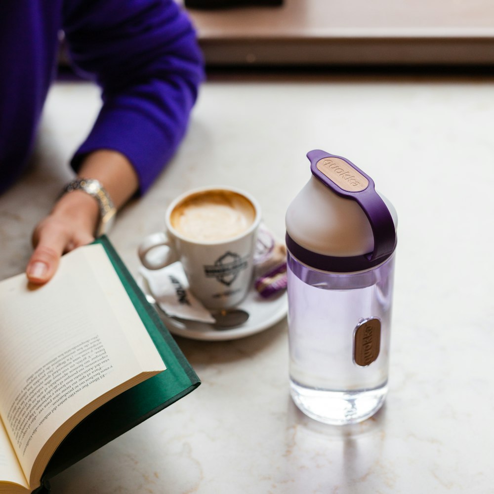 white and purple plastic bottle beside white ceramic mug on white table