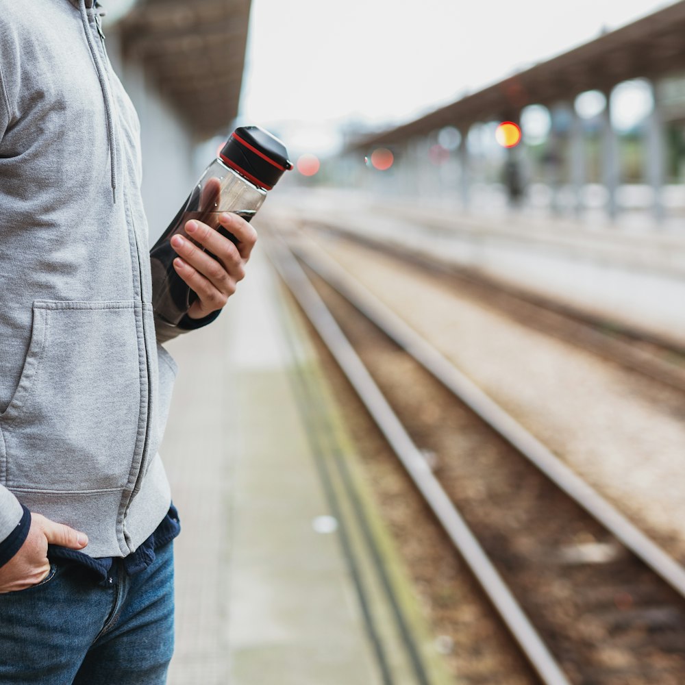 man in gray hoodie and blue denim jeans holding smartphone