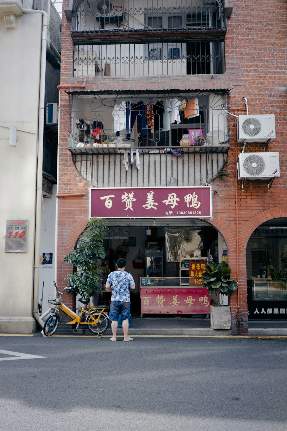 man in blue shirt sitting on brown wooden bench in front of store during daytime