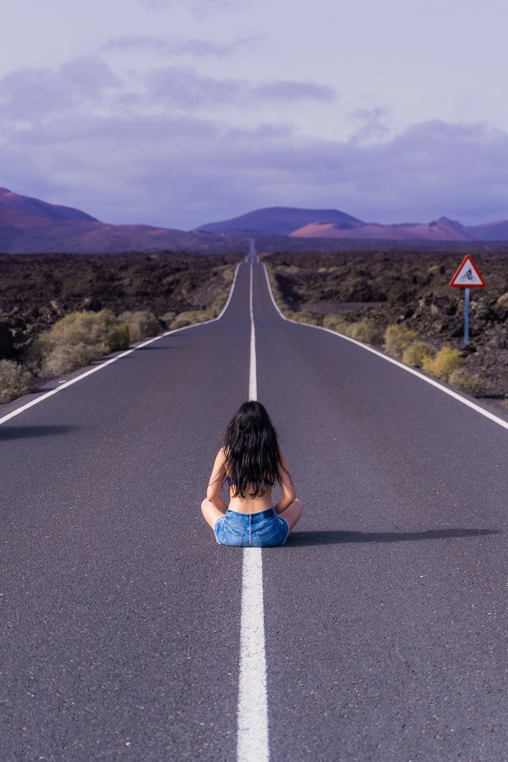 Mujer en chaqueta de mezclilla azul sentada en la carretera durante el día