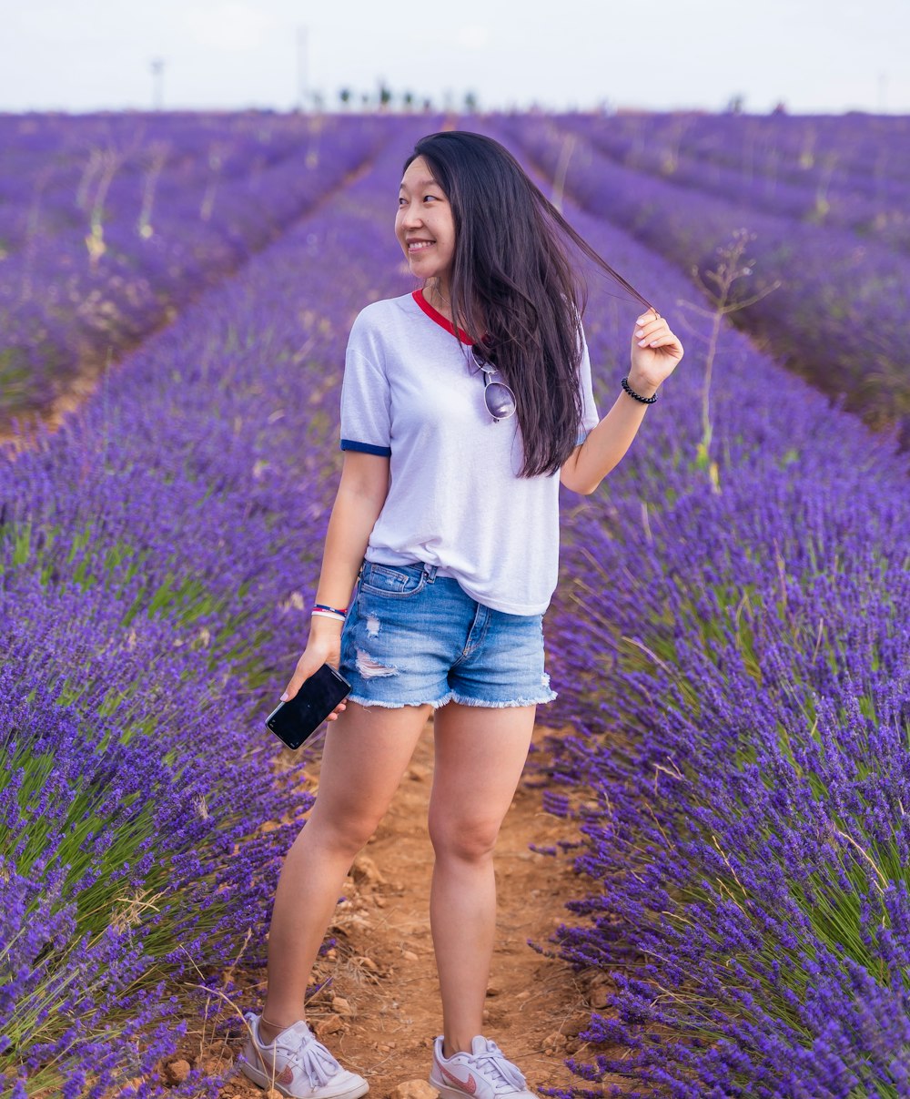 woman in white t-shirt and blue denim shorts standing on purple flower field during daytime