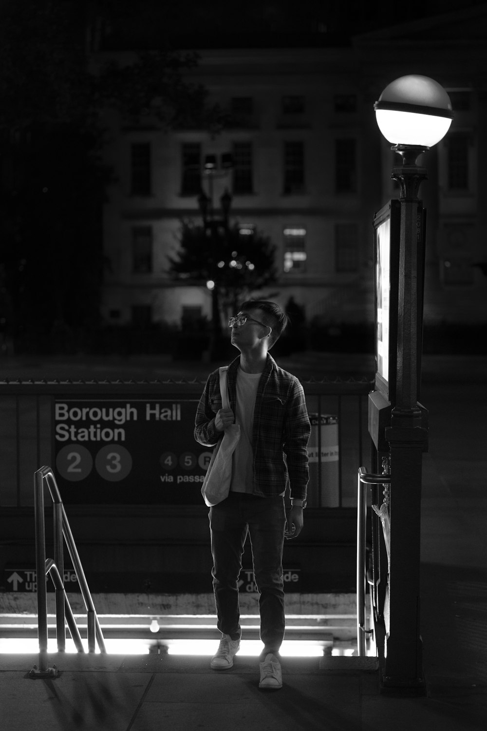 man in suit jacket standing beside street light in grayscale photography
