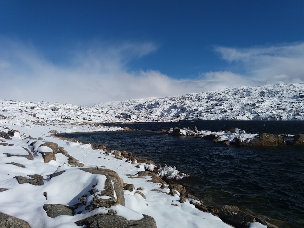 white snow covered rocks near body of water under blue sky during daytime