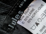 A close-up view of a clothing label showing washing instructions and material composition. The label states the size as 59 cm and the material as 50% wool (laine) and 50% acrylic. Laundry symbols are visible, including one indicating a prohibition against bleaching.