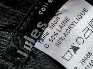 A close-up view of a clothing label showing washing instructions and material composition. The label states the size as 59 cm and the material as 50% wool (laine) and 50% acrylic. Laundry symbols are visible, including one indicating a prohibition against bleaching.