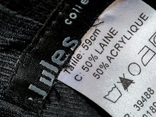 A close-up view of a clothing label showing washing instructions and material composition. The label states the size as 59 cm and the material as 50% wool (laine) and 50% acrylic. Laundry symbols are visible, including one indicating a prohibition against bleaching.
