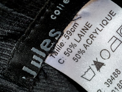 A close-up view of a clothing label showing washing instructions and material composition. The label states the size as 59 cm and the material as 50% wool (laine) and 50% acrylic. Laundry symbols are visible, including one indicating a prohibition against bleaching.