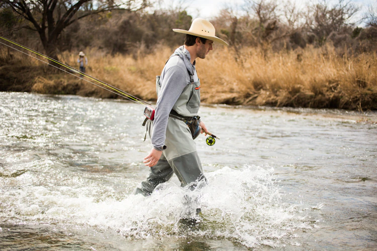 fly fisherman wading fast water with a hat