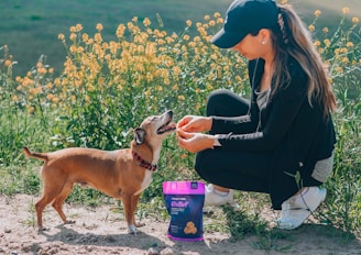 woman in black leather jacket holding purple can beside brown short coated dog