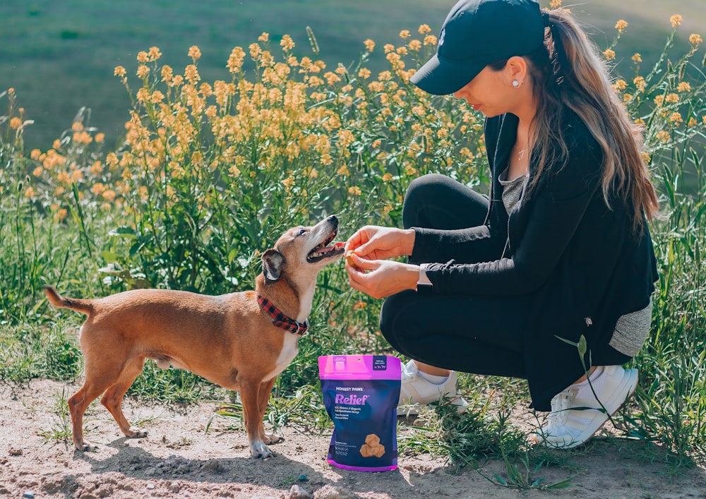 woman in black leather jacket holding purple can beside brown short coated dog