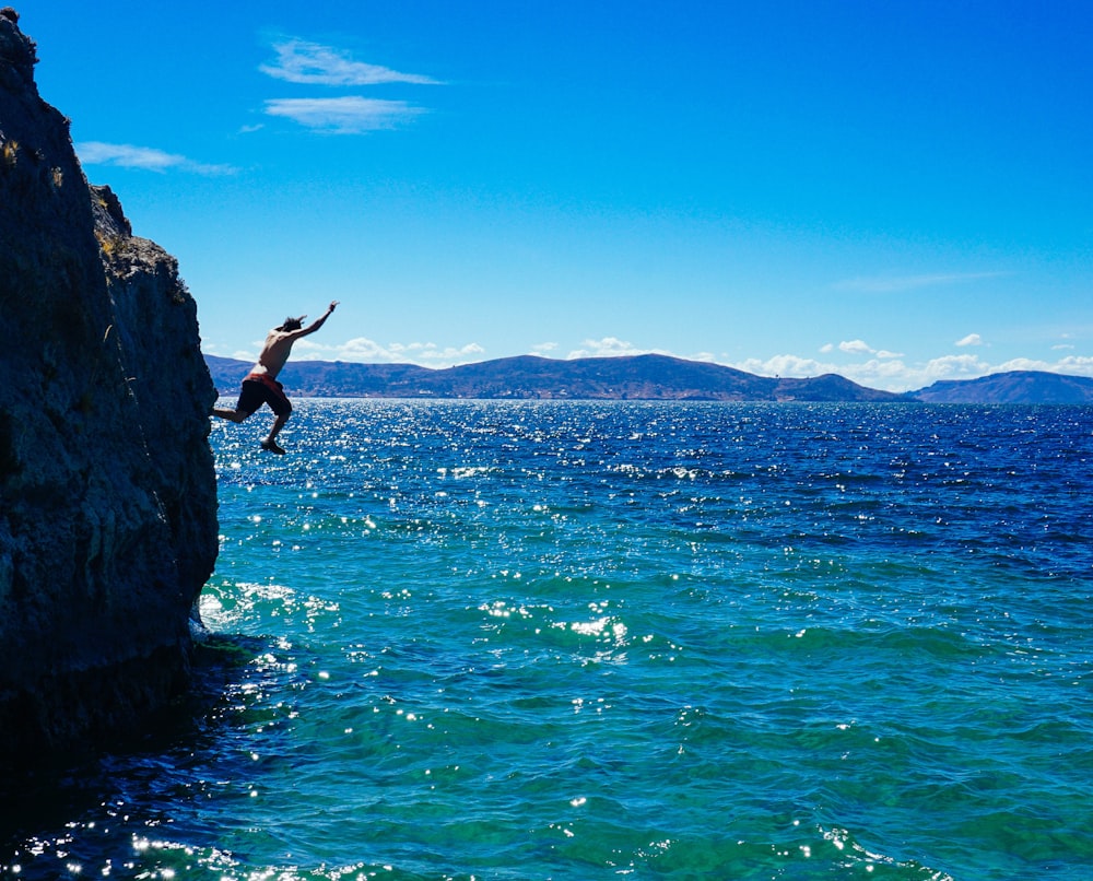 man jumping from cliff to water