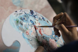 Close-up of a painter's hand mixing Sahra Boya colors on a palette.
