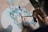 A person is holding a small paintbrush and applying vibrant colors onto a mixing palette. Various shades of blue, pink, red, and green are spread across the palette, suggesting preparation for a creative painting session.