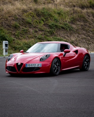 A clean, freshly washed red sports car parked in front of a green leafy backdrop.