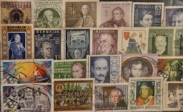 A collection of various vintage postage stamps, mostly from Austria. The stamps feature portraits of notable figures, historic landmarks, and artistic illustrations. Some stamps have been postmarked, indicating they have been used. The arrangement is collage-like, creating a busy and colorful display.