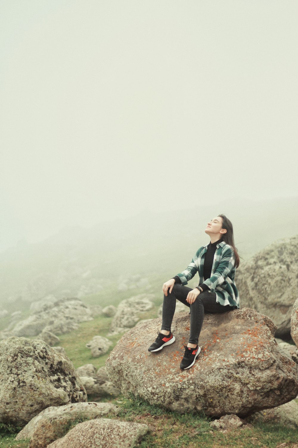 woman in green and black plaid shirt sitting on rock