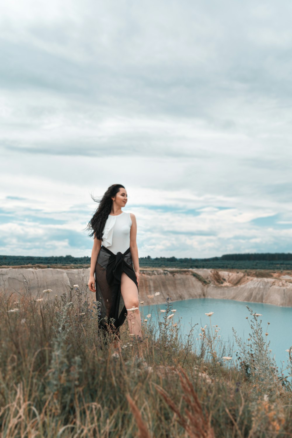 woman in black tank top standing on brown grass field near lake during daytime