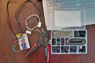 A workspace featuring electronic components including a breadboard with wires connected, a wire cutter or crimping tool, and an organized plastic box with various electronic connectors. Part of a laptop keyboard can also be seen in the corner.
