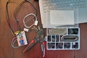 A workspace featuring electronic components including a breadboard with wires connected, a wire cutter or crimping tool, and an organized plastic box with various electronic connectors. Part of a laptop keyboard can also be seen in the corner.