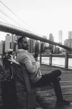 man in gray hoodie sitting on bench in grayscale photography