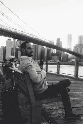 man in gray hoodie sitting on bench in grayscale photography