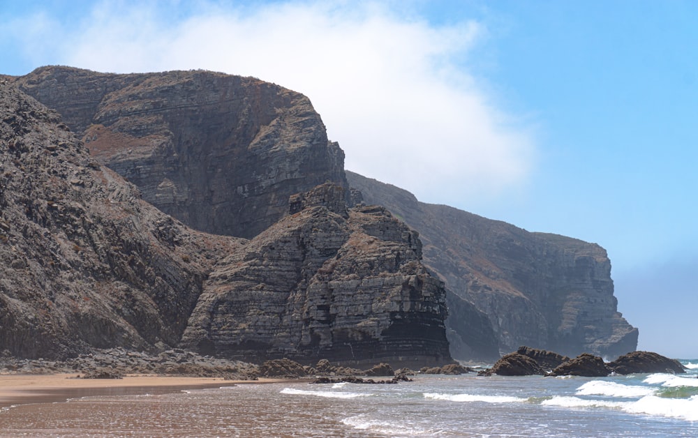 brown rocky mountain beside sea during daytime