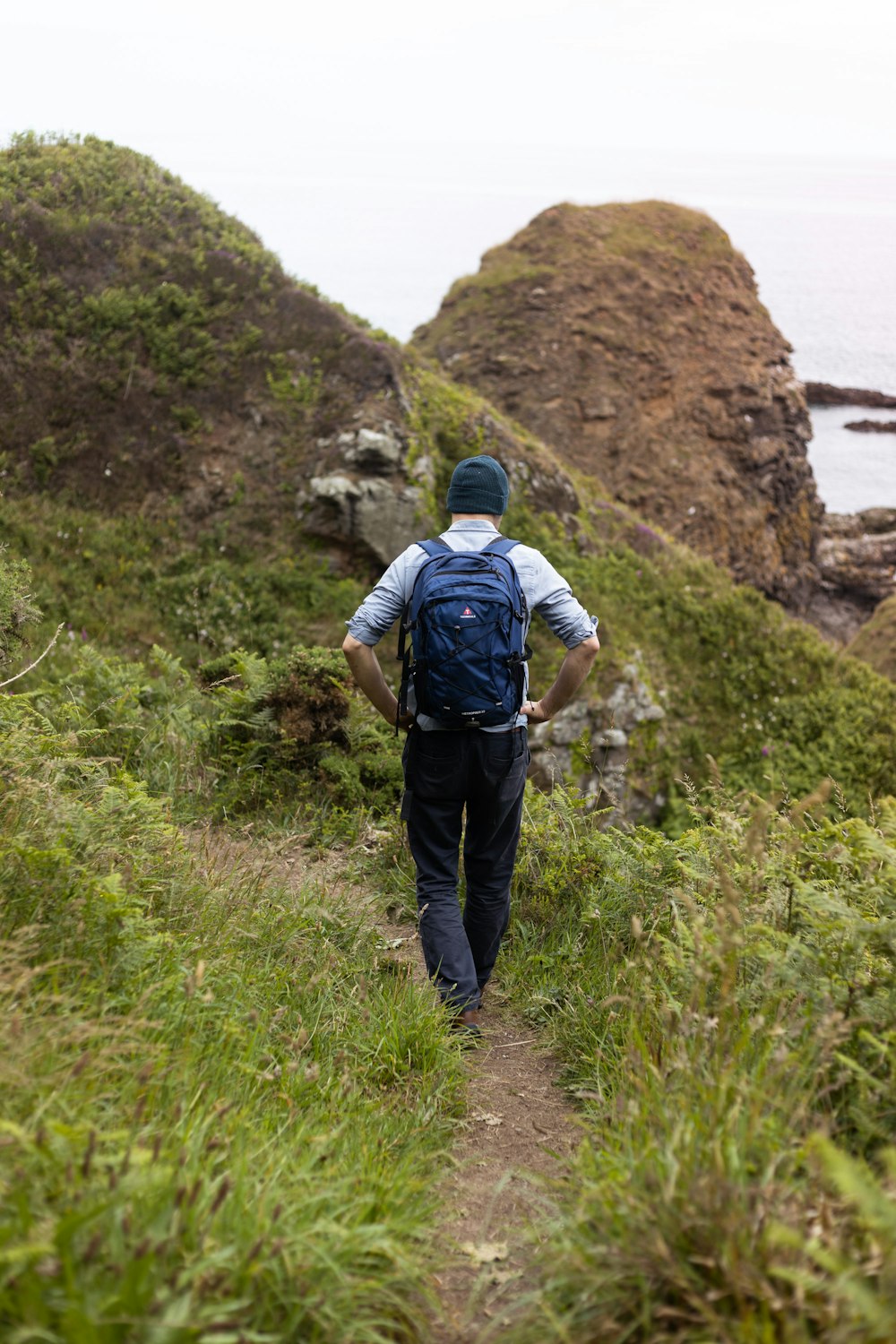 Hombre con camisa azul y pantalones negros con mochila caminando en el campo de hierba verde durante el día