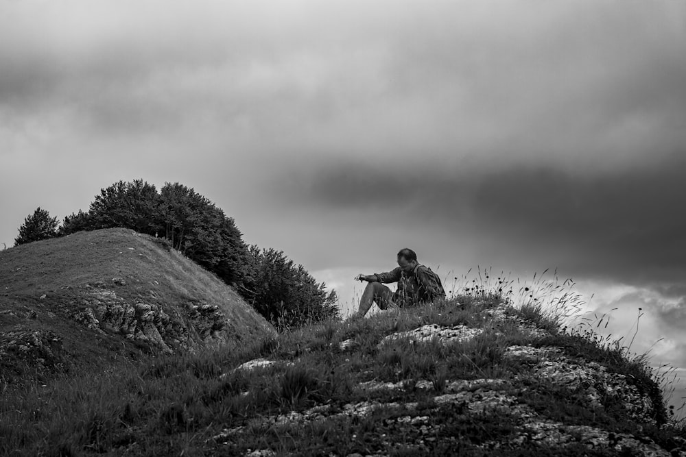 homme en veste grise assis sur le champ d’herbe verte pendant la journée