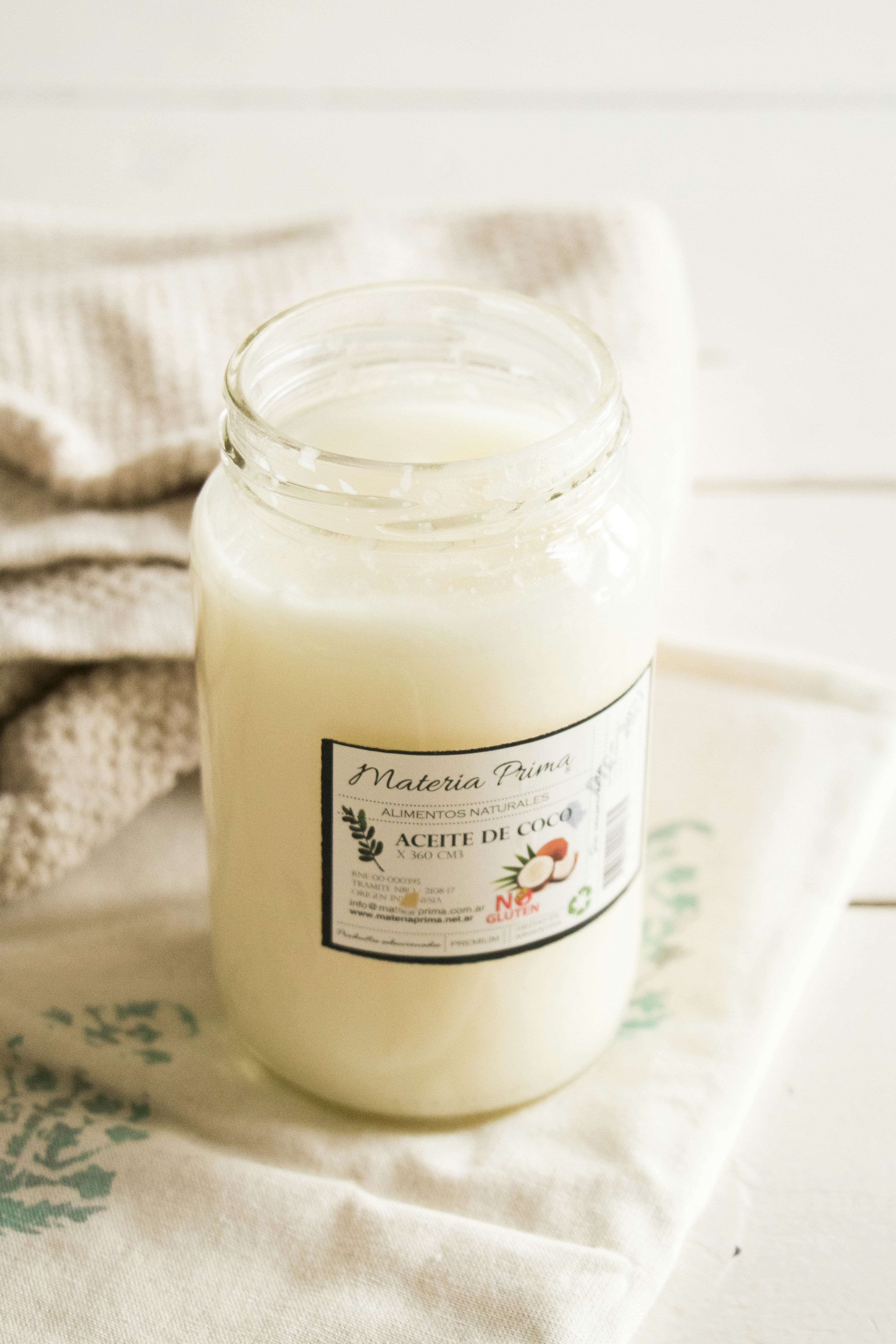 Jar of white coconut oil with coconut halves on tropical background