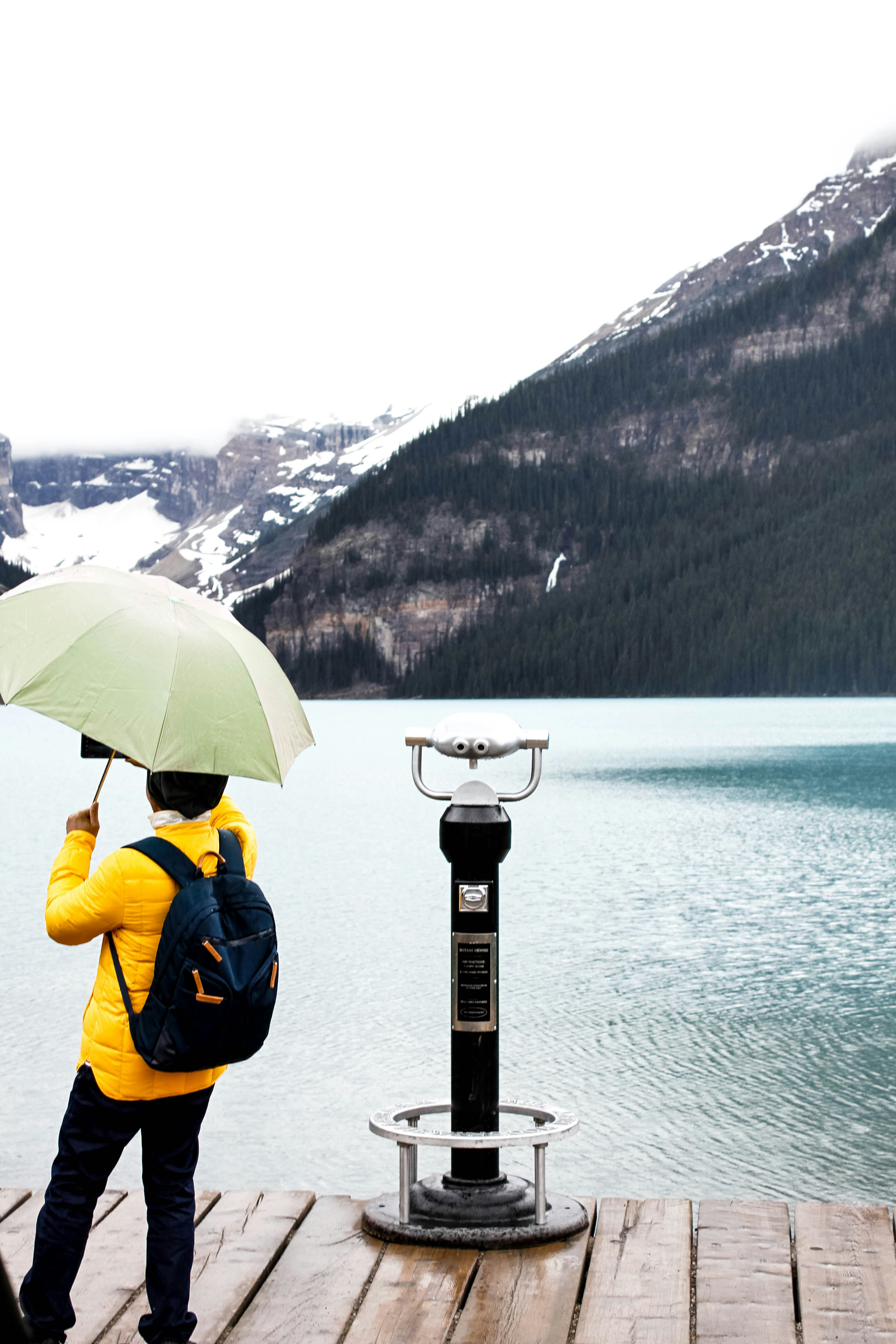 person in yellow jacket holding umbrella standing on dock during daytime