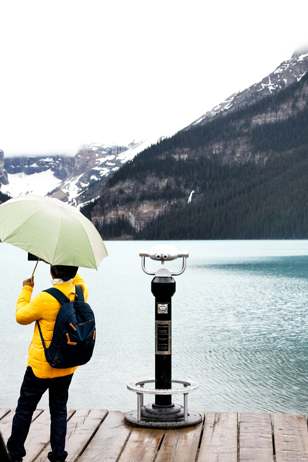 Person in gelber Jacke, die tagsüber einen Regenschirm hält und auf dem Dock steht